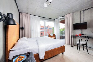 Una habitación de hotel moderna con una cama grande, un escritorio con televisor y un balcón con cortinas.