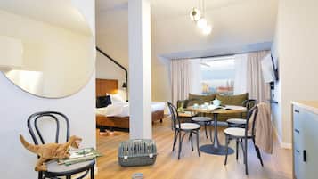 A modern hotel room with a bed, a dining area with a table and chairs, a large mirror, and a view of the city.