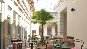 Um café ao ar livre com mesas e cadeiras de madeira, luzes de Natal e uma árvore.