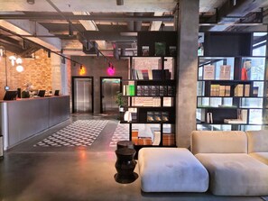 A modern reception area with a check-in counter, a seating area with a sofa and ottoman, a bookshelf with books, and a potted plant. - Dwor Uphagena Arche Gdańsk (Gdańsk)