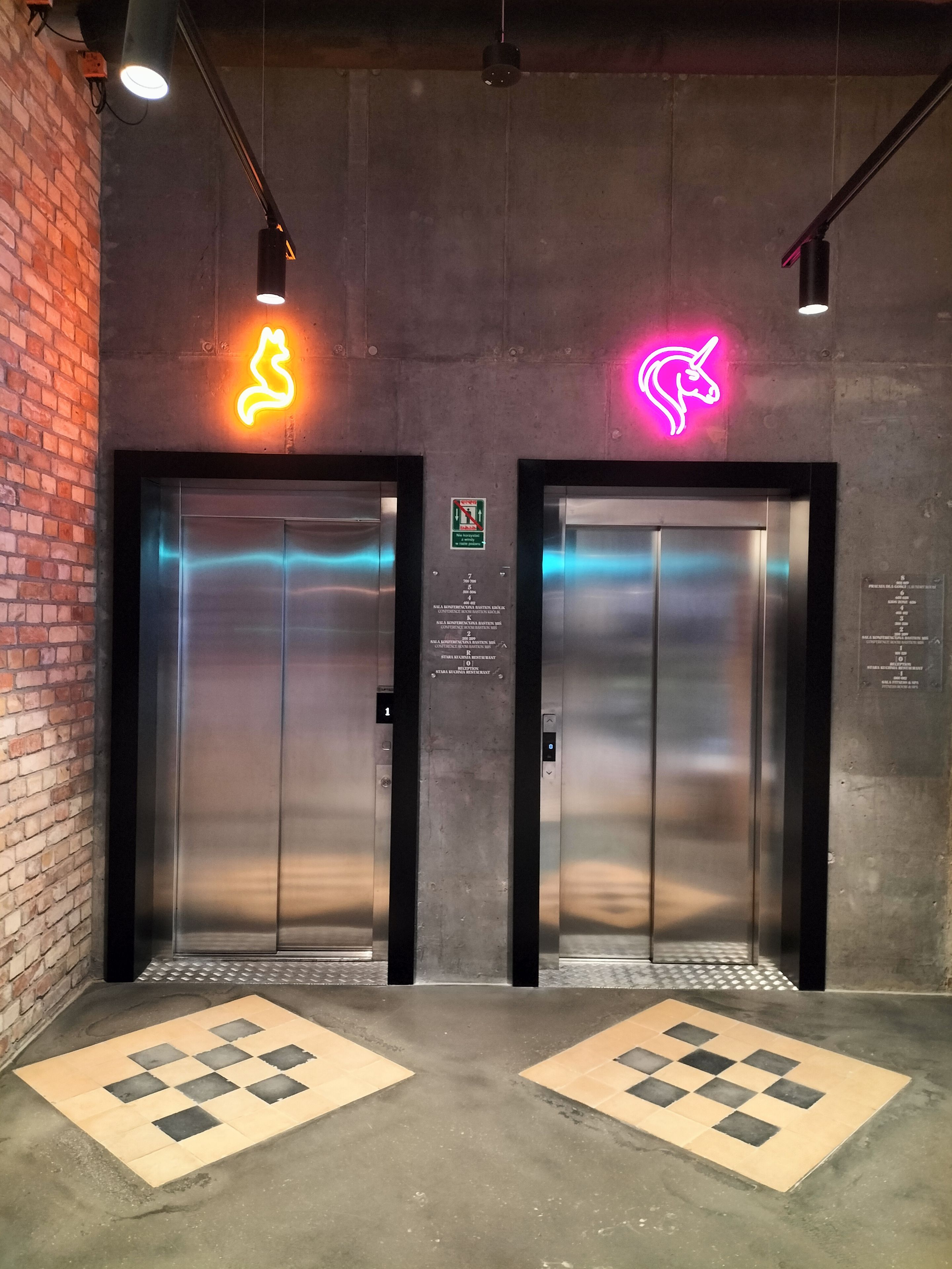 Two elevator doors with neon animal signs, a brick wall, and a checkered floor pattern.