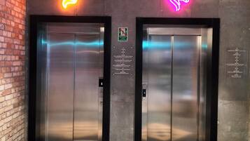 Two elevator doors with neon animal signs, a brick wall, and a checkered floor pattern.