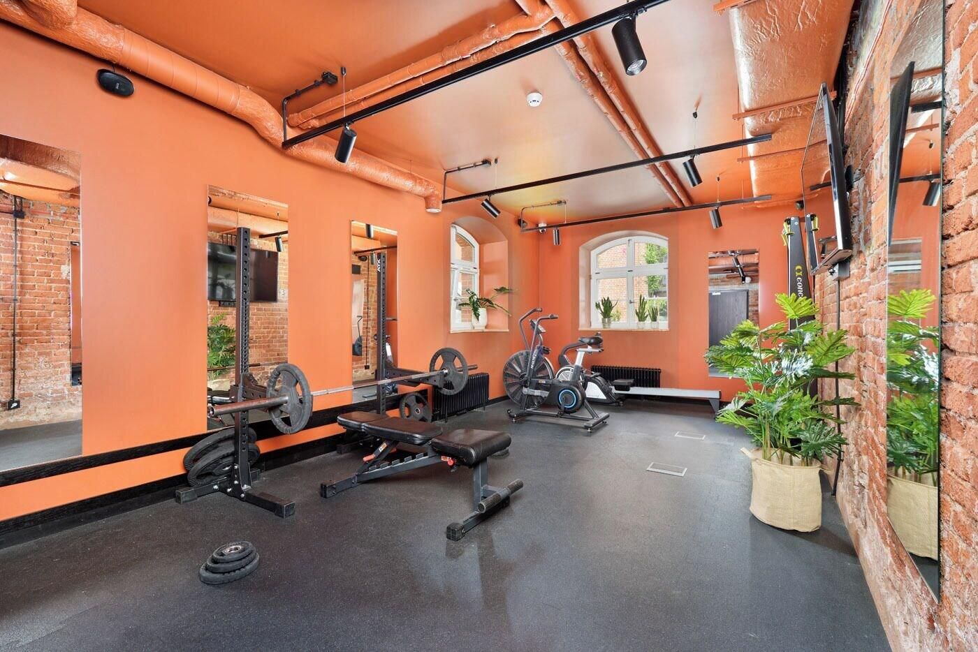 Un gimnasio con equipo de ejercicio, paredes de ladrillo y ventanas amplias.