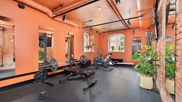 Un gimnasio con equipo de ejercicio, paredes de ladrillo y ventanas amplias.