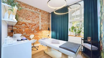 Ein moderner Spa-Raum mit Backsteinwand, einem weißen Empfangstresen, einer Massageliege und einem Fenster mit Vorhängen.