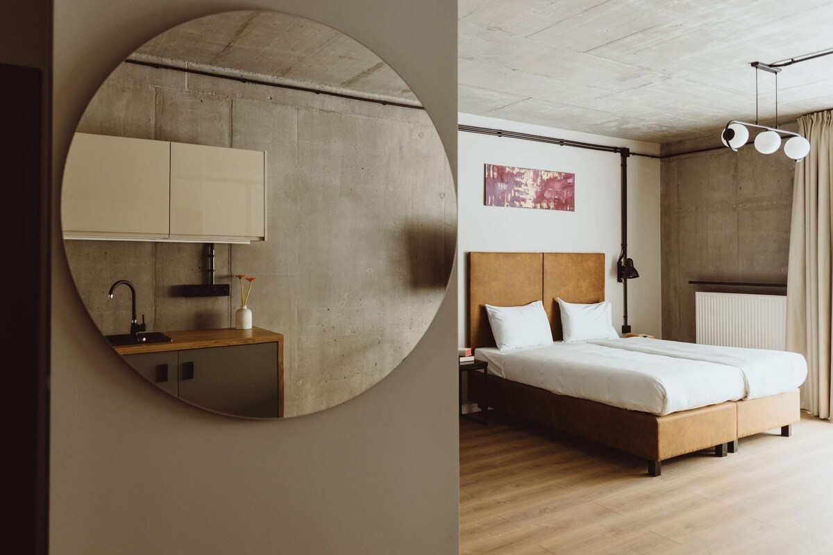 Un dormitorio moderno con una cama de madera, una mesita de noche, una lámpara de pared y un espejo grande.