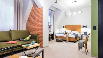 A modern hotel room with a loft-style design, featuring a green sofa, a bed with a wooden headboard, and a small desk area.
