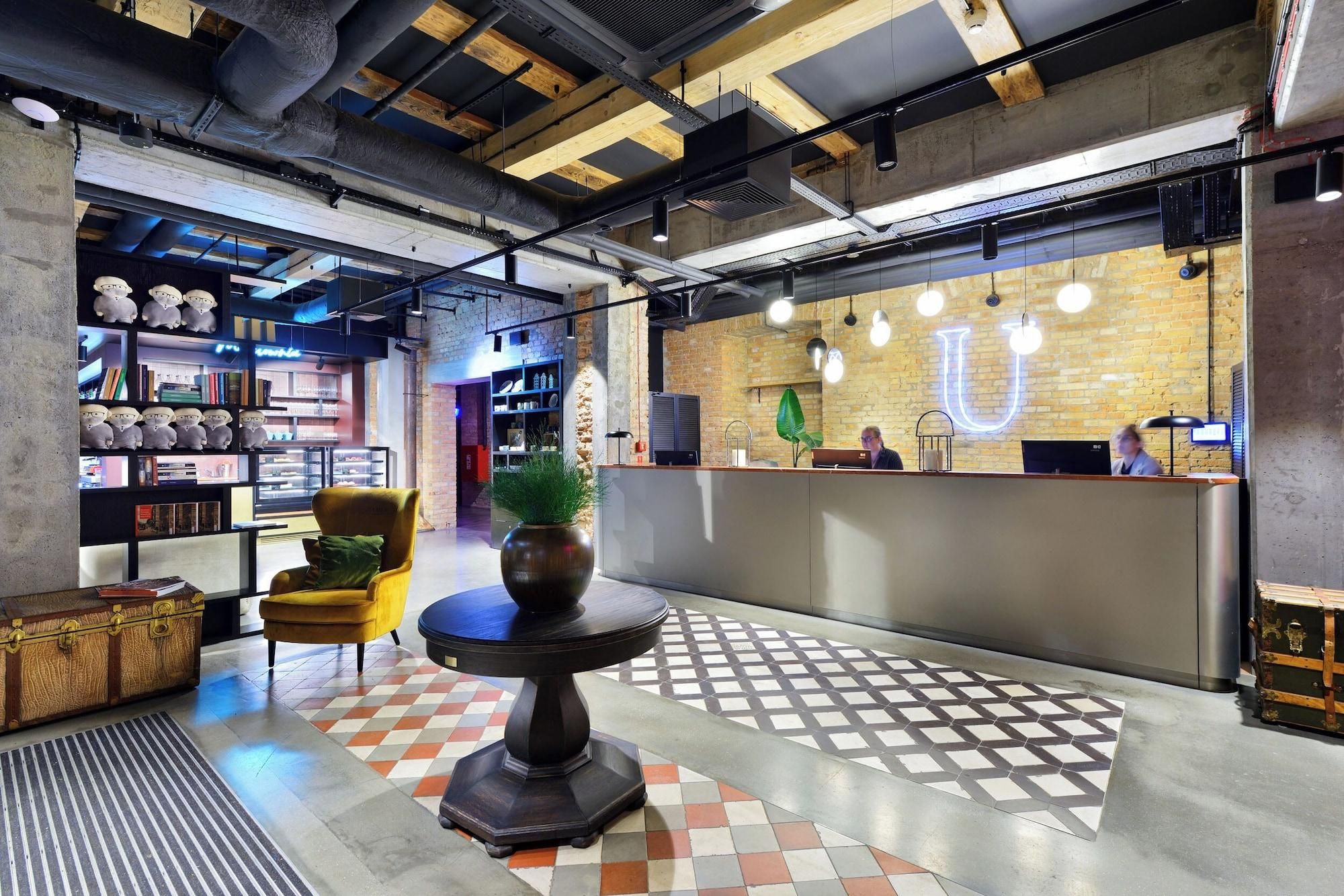 A modern reception area with a check-in counter, a seating area with a round table, and a bookshelf with books and decorative items.