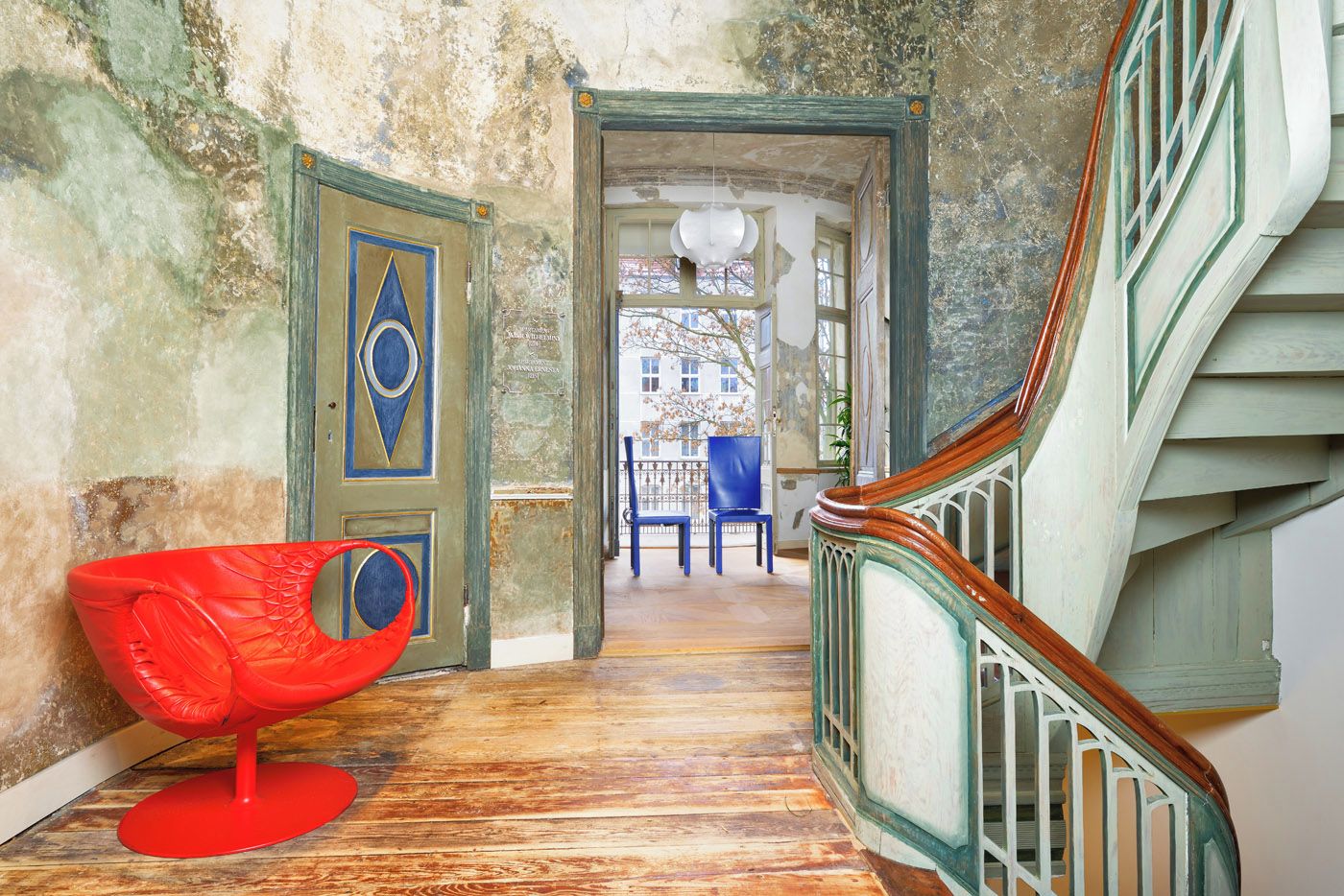 A wooden staircase with a green railing, a red chair, and a door with a blue and gold design.