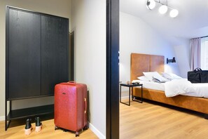 Una habitación de hotel con una cama, una mesita de noche, una maleta y un armario.
