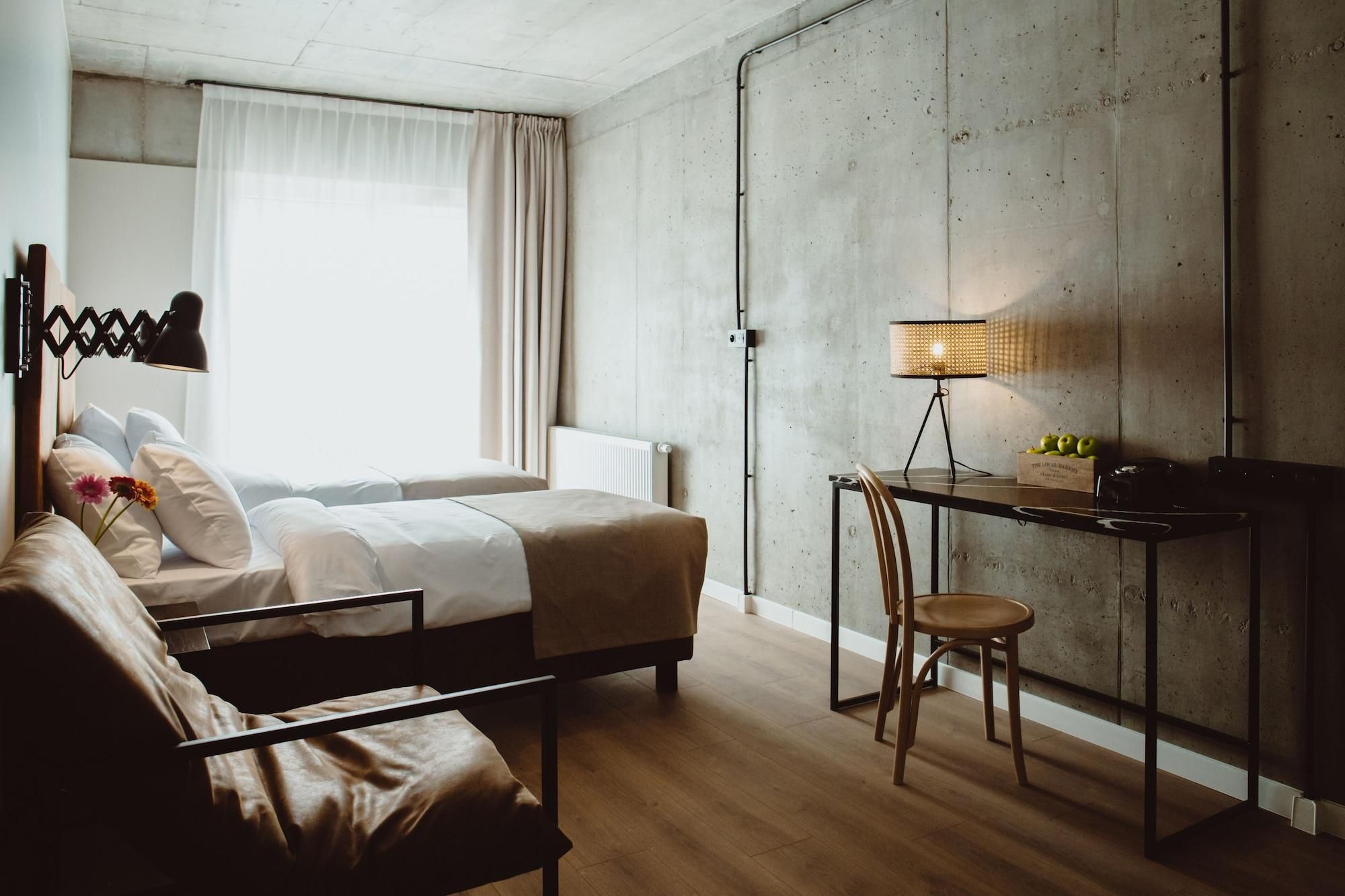 A modern hotel room with a bed, a desk, a chair, and a lamp.