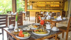 A dining area with multiple tables set for breakfast, including plates of food, a croissant, and a fruit salad. - Sakti Garden Resort & Spa (Ubud)