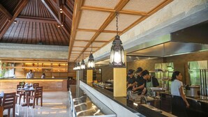 A restaurant with a long counter, hanging lanterns, and a kitchen area with staff preparing food. - Sakti Garden Resort & Spa (Ubud)