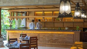 A restaurant with a wooden bar and seating area, featuring a stone wall and greenery. - Sakti Garden Resort & Spa (Ubud)