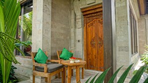 A wooden door with intricate carvings, a stone wall, and a small round table with a cushion and a vase of flowers. - Sakti Garden Resort & Spa (Ubud)