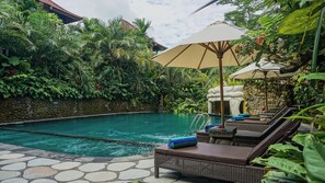 A pool area with lounge chairs, a stone wall, and lush greenery. - Sakti Garden Resort & Spa (Ubud)