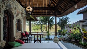 A room with a bed, a table, and chairs. There is a view of a garden and a body of water outside. - Sakti Garden Resort & Spa (Ubud)
