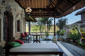 A room with a bed, a table, and chairs. There is a view of a garden and a body of water outside. - Sakti Garden Resort & Spa (Ubud)