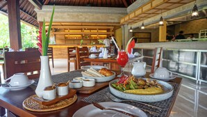 A dining area with a table set for two, featuring a variety of dishes, a fruit drink, and a vase with flowers. - Sakti Garden Resort & Spa (Ubud)