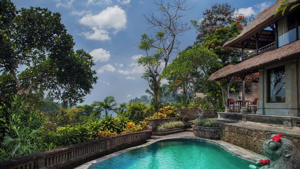 A swimming pool surrounded by lush greenery and a thatched-roof building. - Sakti Garden Resort & Spa (Ubud)