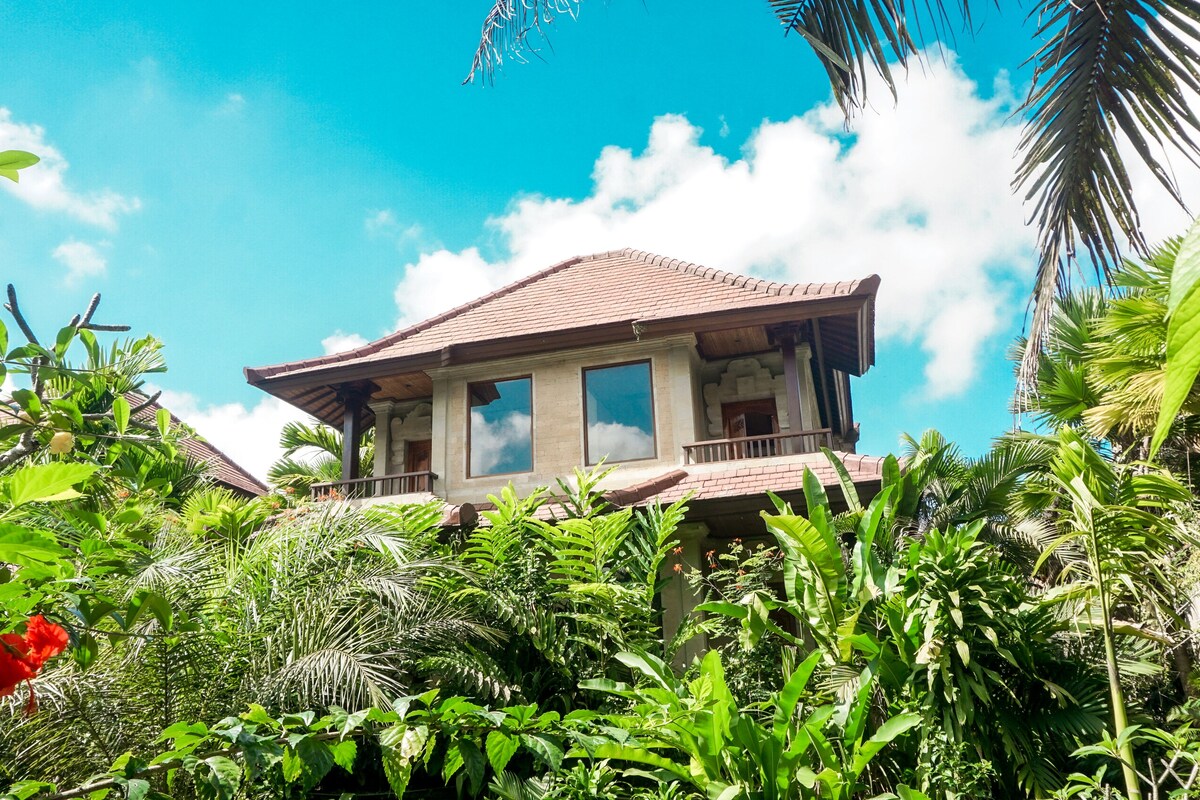 A traditional two-story building with a tiled roof, surrounded by lush tropical vegetation.