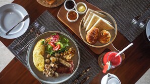 A breakfast setting with a plate of eggs, mushrooms, bacon, and salad, a plate of croissants, and a glass of watermelon smoothie. - Sakti Garden Resort & Spa (Ubud)