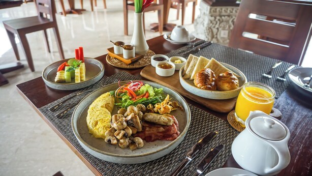 A breakfast setting with plates of food, including eggs, sausages, and vegetables, along with a glass of orange juice. - Sakti Garden Resort & Spa (Ubud)