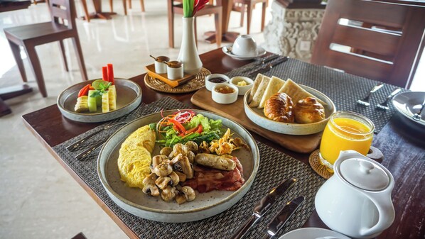 A breakfast setting with plates of food, including eggs, sausages, and vegetables, along with a glass of orange juice. - Sakti Garden Resort & Spa (Ubud)
