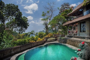 A swimming pool surrounded by lush greenery and a thatched-roof building. - Sakti Garden Resort & Spa (Ubud)