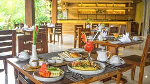 A dining area with multiple tables set for breakfast, including plates of food, a croissant, and a fruit salad. - Sakti Garden Resort & Spa (Ubud)