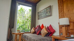 A room with a bed, a small table with a bowl of fruit, a lamp, and a painting on the wall. - Sakti Garden Resort & Spa (Ubud)