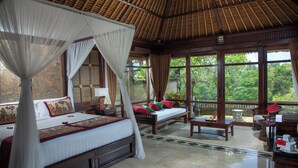 A spacious bedroom with a large bed, a sitting area, and a balcony with a view of the greenery. - Sakti Garden Resort & Spa (Ubud)