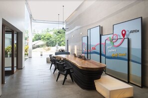 A modern reception area with a wooden reception desk, black chairs, and a glass wall with a map design. - Jonox Phuket Karon (Karon)