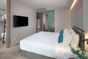 A modern hotel room with a large bed, a flat-screen TV mounted on the wall, a walk-in closet, and a bathroom visible through an open door. - Jonox Phuket Karon (Karon)