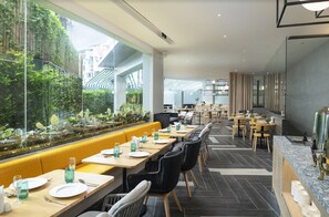 Un restaurant moderne avec de longues tables, des banquettes jaunes et une vue sur la verdure grâce à de grandes fenêtres.