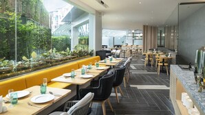 A modern restaurant with long tables, yellow booths, and a view of greenery through large windows. - Jonox Phuket Karon (Karon)