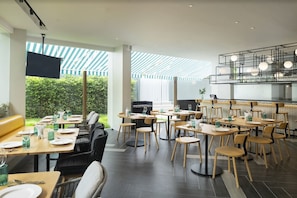 A modern restaurant with a mix of seating options, including tables and chairs, and a large TV screen. - Jonox Phuket Karon (Karon)