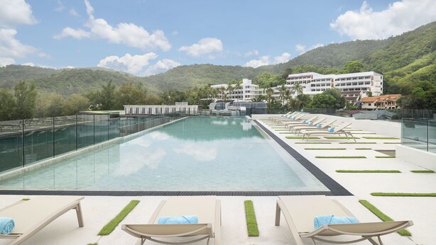 A swimming pool with lounge chairs and a view of a hillside building. - Jonox Phuket Karon (Karon)