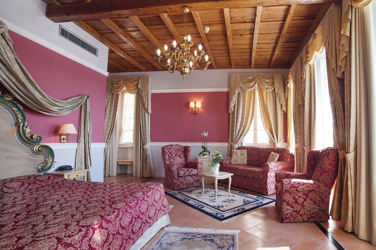 A room with a bed, two armchairs, a small table, and a chandelier.