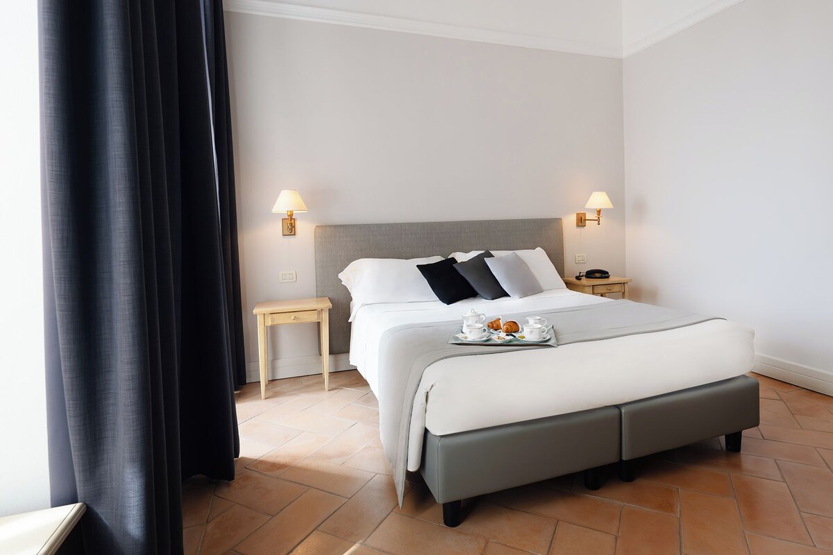 A neatly arranged hotel room with a bed, bedside tables, and a tray of breakfast items.