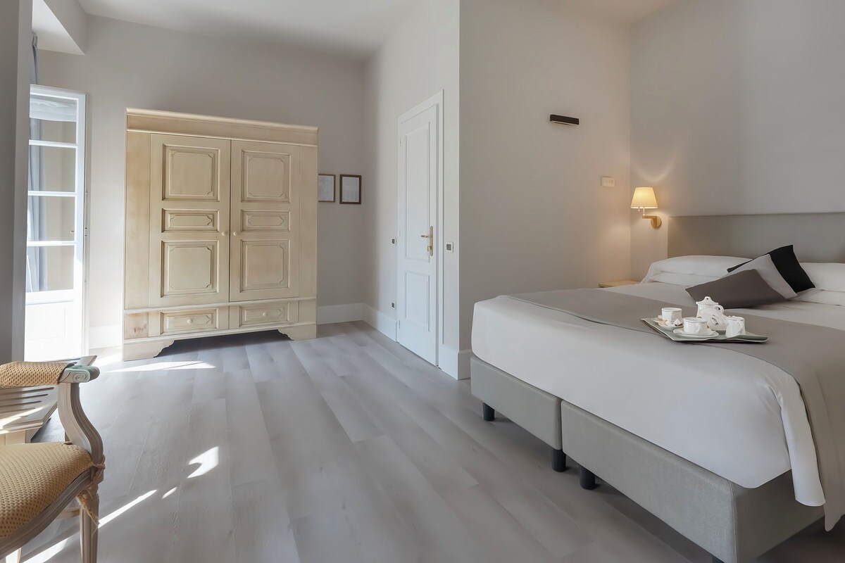 A hotel room with a large bed, bedside tables, a wardrobe, and a chair.