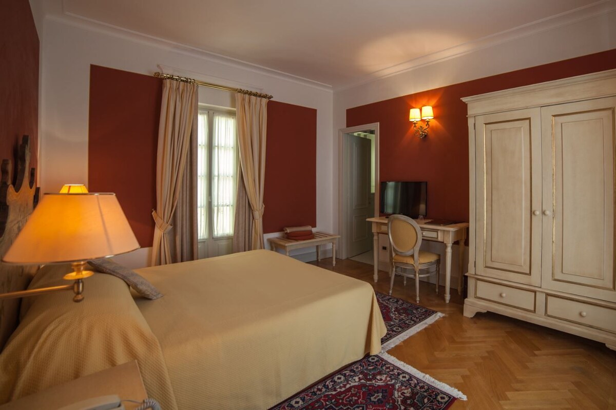 A hotel room with a bed, desk, wardrobe, and a lamp.