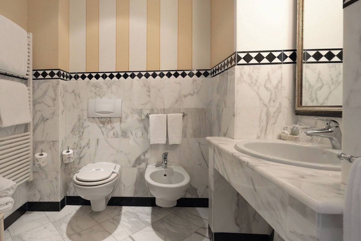A bathroom with a toilet, bidet, and sink, all with marble countertops.