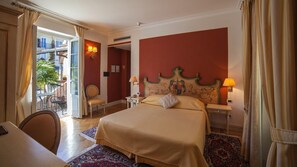 A hotel room with a large bed, two bedside tables, a chair, and a balcony with a view of buildings. - Hotel Cannero (Cannero Riviera)