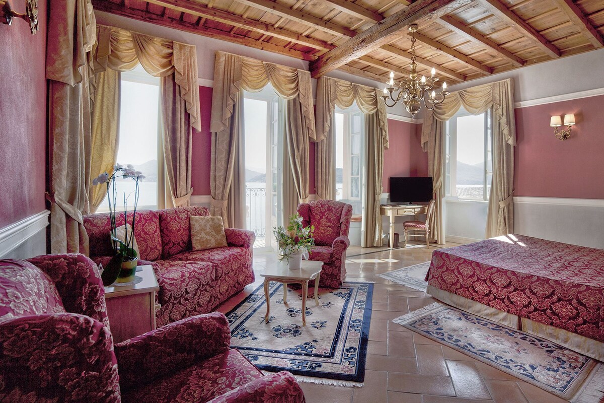 A room with a wooden ceiling, a sofa, a chair, a small table with a vase, and a bed.
