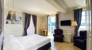 Une chambre d’hôtel avec un lit, deux fauteuils, un bureau avec une lampe, une télévision et une vue sur l’extérieur.