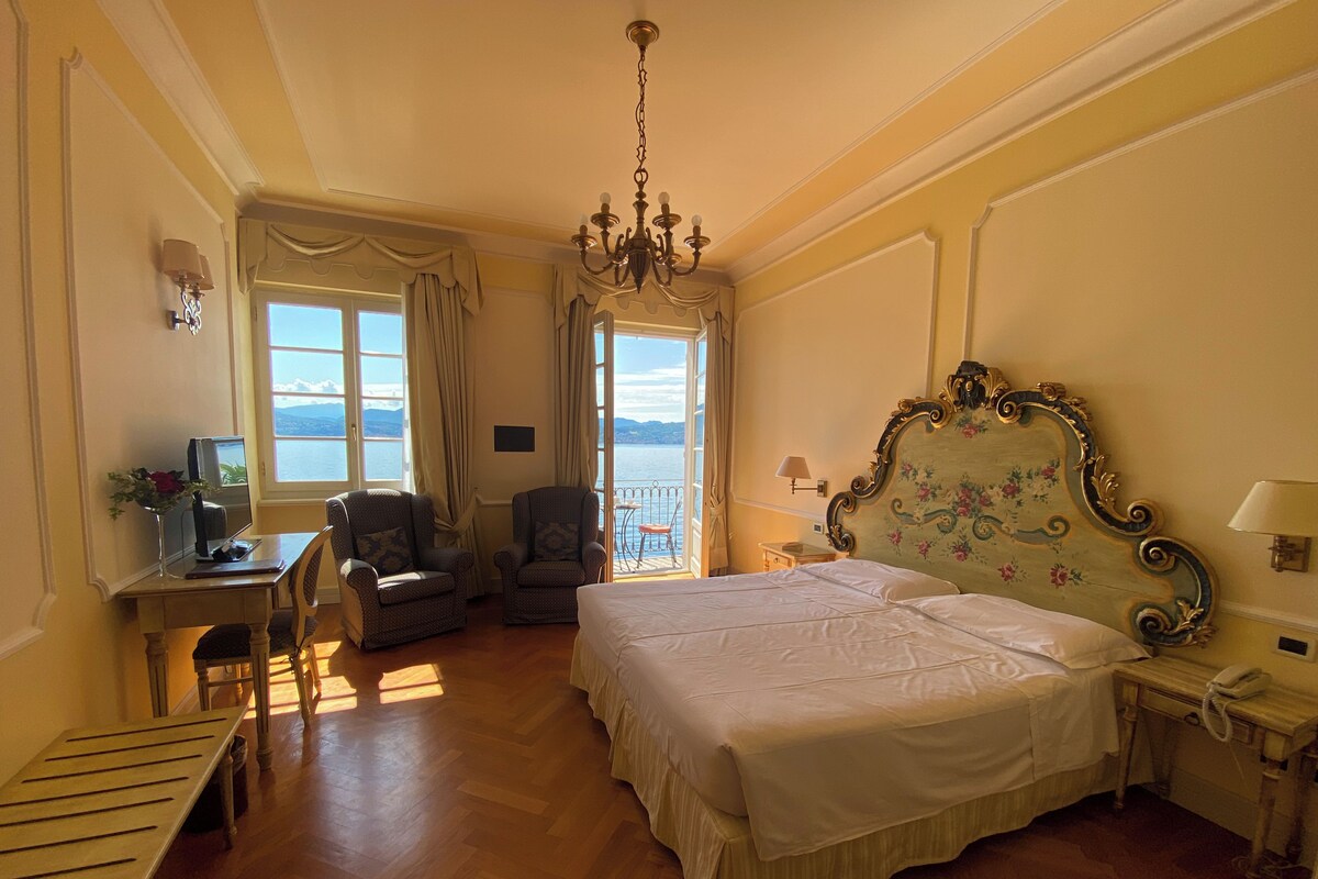 A hotel room with a large bed, a desk with a computer, a chair, and a view of the sea.