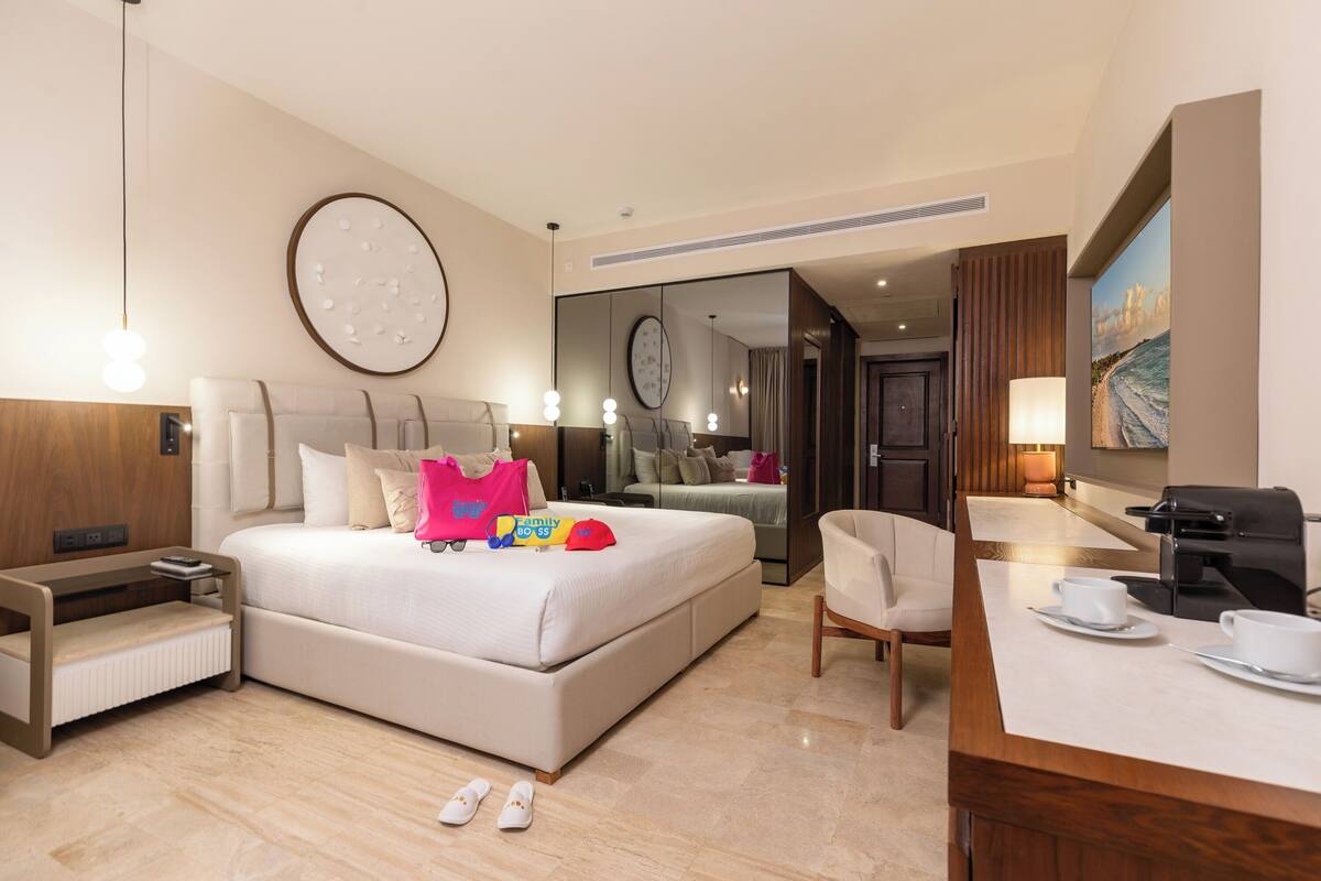 Una habitación de hotel moderna con una cama grande, mesitas de noche, un escritorio con cafetera y vista al océano.