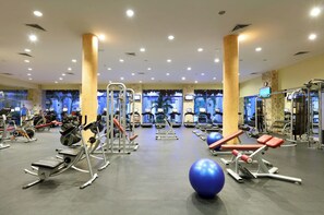 Ein Fitnessstudio mit verschiedenen Trainingsgeräten, darunter Laufbänder, Kraftgeräte und Kurzhanteln.