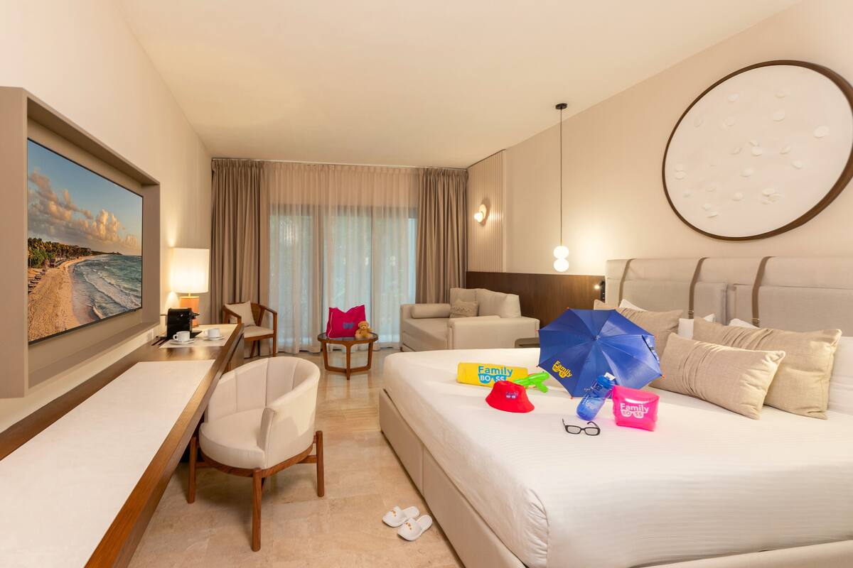 Habitación de hotel con cama, escritorio, silla, televisor y ventana con cortinas.